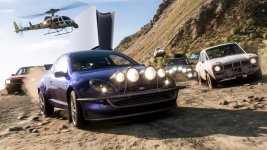 Das Bild zeigt eine dynamische Szene aus dem Open-World-Rennspiel Forza Horizon 5. Im Vordergrund ist ein sportliches Auto mit mehreren Scheinwerfern zu sehen, das auf einer staubigen Strecke fährt. Um das Auto herum sind weitere Fahrzeuge, die ebenfalls an dem Rennen teilnehmen. Im Hintergrund fliegt ein Helikopter, während sich Hügel und eine lebendige Landschaft abzeichnen. Diese Szenerie vermittelt ein Gefühl von Geschwindigkeit und Abenteuer, passend zur aufregenden Atmosphäre des Spiels.