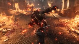 Das Bild zeigt eine beeindruckende Szene aus einem düsteren Action-Adventure-Spiel. Im Vordergrund ist eine lebendige Puppe zu sehen, die mit einem Schwert kämpft. Sie ist von mitreißenden energetischen Effekten umgeben, die den Eindruck von Bewegung und Intensität vermitteln. Im Hintergrund sind Flammen und Zerstörung wahrzunehmen, was auf eine chaotische Umgebung hindeutet. Die gesamte Atmosphäre des Bildes ist düster und aggressiv, was die Stimmung des Spiels Zeugn ist. Die Verwendung von Licht und Schatten verstärkt die dramatische Wirkung der Szene.