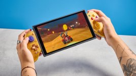 Das Bild zeigt eine Person, die einen farbenfrohen Controller in der Hand hält und auf einen Bildschirm schaut, auf dem ein Spiel abgebildet ist. Der Hintergrund ist in einem hellen Blau gestaltet, während die Szene insgesamt eine entspannte und spielerische Atmosphäre ausstrahlt. Der Controller und das Handheld-Gerät heben sich gut vom Hintergrund ab und vermitteln ein Gefühl von Modernität und Technologie. Die Person scheint in das Spiel vertieft zu sein und genießt das Erlebnis der mobilen Spiele.