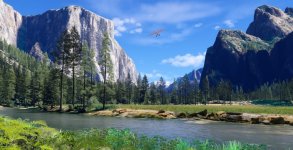 Das Bild zeigt eine atemberaubende Landschaft mit hohen Bergen und üppigen, grünen Wäldern. In der Mitte fließt ein ruhiger Fluss, der von großen Felsen gesäumt wird. Am Himmel ist ein kleines Flugzeug zu sehen, das über die Landschaft fliegt. Der Himmel ist strahlend blau und mit einigen weißen Wolken verziert, was der Szenerie eine friedliche und erlebnisreiche Atmosphäre verleiht. Die natürliche Schönheit des Aufnahmen vermittelt ein Gefühl von Freiheit und Abenteuer in der Luftfahrt.