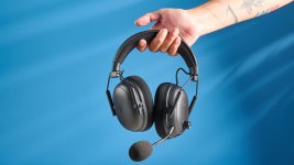 Das Bild zeigt ein hochwertiges Gaming-Headset, das von einer Hand gehalten wird. Das Headset hat eine schwarz-graue Farbgebung und zeichnet sich durch bequeme Ohrpolster sowie ein abnehmbares Mikrofon aus. Der Hintergrund ist in einem hellen Blau gehalten, was dem Bild Frische und Dynamik verleiht. Das Headset wirkt modern und professionell, ideal für Gaming-Enthusiasten, die Wert auf Soundqualität legen.