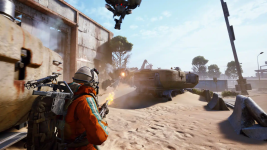 Das Bild zeigt eine dynamische Spielsituation aus dem Spiel ARC Raiders. Im Vordergrund ist ein Protagonist zu sehen, der in einem orangefarbenen Anzug mit einem Rucksack und einem Gewehr bewaffnet ist. Er steht auf einem sandigen Boden, während im Hintergrund eine destruktive Umgebung mit verlassenen Fahrzeugen, zerfallenen Gebäuden und einer noch aktiven Zerstörung sichtbar ist. Darüber schwebt ein Drohnen-ähnliches Objekt, das anscheinend eine Attacke ausführt oder Unterstützung bietet. Die Szene vermittelt ein Gefühl von Action und Abenteuer in einer post-apokalyptischen Welt, angereichert durch eine klare, helle Tageslichtatmosphäre.