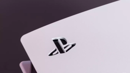 Das Bild zeigt eine PlayStation-Konsole aus einer nahen Perspektive, bei der das markante PlayStation-Logo sichtbar ist. Die Konsole hat ein modernes, minimalistisches Design in einer hellen Farbe und setzt auf eine glatte Oberfläche. Der Hintergrund ist in einem dunkleren Farbton gehalten, was einen Kontrast zur Konsole bildet und die Aufmerksamkeit auf das Logo lenkt. Dieses Bild könnte die Vorfreude und das Interesse an der kommenden PlayStation 6 symbolisieren, während es gleichzeitig Fragen zur aktuellen Konsolengeneration aufwirft.