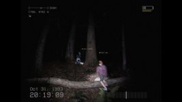 Das Bild zeigt eine düstere Waldszene, die in der Nacht aufgenommen wurde. Zwei Personen sind im Vordergrund zu sehen, wobei die eine Person hinter einem Baum versteckt ist und die andere sich auf einem Baumstamm bewegt. Der Hintergrund ist von hohen Bäumen und dunkler Umgebung geprägt, was eine gruselige Atmosphäre schafft. Die Bildqualität erinnert an eine alte Webcam- oder Überwachungsaufnahme und trägt zur unheimlichen Stimmung bei. Ein Datum und eine Uhrzeit in der unteren Ecke deuten auf den 31. Oktober 1993 hin, was den Halloween-Kontext verstärkt. Das Bild zeigt eine düstere Waldszene, die in der Nacht aufgenommen wurde. Zwei Personen sind im Vordergrund zu sehen, wobei die eine Person hinter einem Baum versteckt ist und die andere sich auf einem Baumstamm bewegt. Der Hintergrund ist von hohen Bäumen und dunkler Umgebung geprägt, was eine gruselige Atmosphäre schafft. Die Bildqualität erinnert an eine alte Webcam- oder Überwachungsaufnahme und trägt zur unheimlichen Stimmung bei. Ein Datum und eine Uhrzeit in der unteren Ecke deuten auf den 31. Oktober 1993 hin, was den Halloween-Kontext verstärkt.