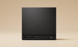 Das Bild zeigt eine kompakte, schwarze Gaming-Konsole im minimalistischen Design. Sie hat eine rechteckige Form mit abgerundeten Kanten und wirkt insgesamt sehr modern und stilvoll. An der Vorderseite sind zwei USB-Anschlüsse sowie ein microSD-Slot zu sehen. In der Ecke befindet sich ein runder Knopf mit einer kleinen LED-Anzeige. Der Hintergrund ist in einem neutralen Beige gehalten, was der Konsole einen eleganten Kontrast verleiht. Die gesamte Erscheinung vermittelt den Eindruck von Hochwertigkeit und technischer Raffinesse, ideal für ein modernes Wohnzimmer-Setup.