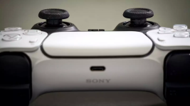 Das Bild zeigt einen PlayStation 5 Controller in Nahaufnahme. Die Vorderseite des Controllers ist gut sichtbar, einschließlich der beiden Joysticks und der Tasten. Der Controller hat ein modernes, ergonomisches Design mit einer Kombination aus Weißen und Schwarzen Elementen. In der Mitte befindet sich ein USB-C Anschluss, was auf die zeitgemäße Technologie des Geräts hinweist. Der Hintergrund ist unscharf und hell, wodurch der Fokus ganz klar auf dem Controller liegt, der für Gamer ein zentrales Element beim Spielen darstellt.