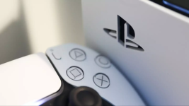 Das Bild zeigt eine PlayStation 5 Konsole mit einem Controller im Vordergrund. Die Konsole hat ein elegantes Design mit einer markanten weißen und schwarzen Farbgebung. Auf dem Controller sind die typischen Bedienelemente klar erkennbar, einschließlich der bekannten Symboltasten. Im Hintergrund ist das PlayStation-Logo zu sehen, das sich im Gehäuse der Konsole befindet. Die Bildkomposition vermittelt eine moderne und technologische Atmosphäre, die die Beliebtheit und das Interesse an Gaming-Geräten unterstreicht.