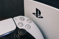 Das Bild zeigt einen Teil einer PlayStation 5 Slim Konsole zusammen mit einem Controller. Die Konsole hat eine schlanke, moderne Form und ist in einem eleganten Weiß gehalten. Besonders auffällig ist das Logo von PlayStation, das auf der Konsole abgebildet ist. Neben dem Logo sind einige Tasten des Controllers zu sehen, die gängige Symbole wie ein Quadrat, ein Kreis und ein Kreuz zeigen. Insgesamt vermittelt das Bild einen Eindruck von moderner Gaming-Technologie und intuitivem Design.
