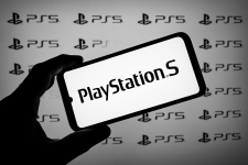 Auf dem Bild ist ein Smartphone zu sehen, das in einer Hand gehalten wird. Auf dem Bildschirm zeigt es das Logo der PlayStation 5 in großen Buchstaben. Im Hintergrund sind mehrfach wiederholte PlayStation 5 Logos zu erkennen, die in einer monochromen Farbgestaltung gehalten sind. Das gesamte Bild vermittelt einen modernen und technologischen Eindruck, der sich gut in den Kontext von Gaming und der PlayStation 5 einfügt.