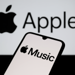 Das Bild zeigt ein Smartphone, auf dessen Display das Logo von Apple Music zu sehen ist. Im Hintergrund ist das bekannte Apple-Logo zu erkennen. Die Farben sind in neutralen Tönen gehalten, was eine moderne und schlichte Ästhetik vermittelt. Der Fokus liegt auf der App von Apple Music, die dem Betrachter ins Auge fällt, während das Apple-Logo dezent im Hintergrund erscheint. Dieses Bild könnte im Kontext von Musikstreaming oder digitalen Angeboten genutzt werden, um die Verbindung zwischen Apple Produkten und Musikdiensten zu symbolisieren.
