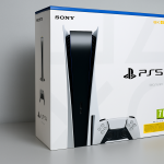 Das Bild zeigt die Verpackung einer PlayStation 5. Die Box ist in überwiegend weißen und blauen Farben gehalten und zeigt das PS5-Logo sowie das Design der Konsole, das für seine schlanke, futuristische Form bekannt ist. Auf der Vorderseite sind auch das PlayStation-Controller-Symbol und Altersfreigaben sichtbar. Die Verpackung wirkt modern und ansprechend, was die Vorfreude auf den Inhalt, die Konsole, unterstreicht.