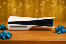 Das Bild zeigt eine stilvolle PlayStation 5 Konsole, die auf einem blauen Tisch platziert ist. Die Konsole hat ein elegantes, futuristisches Design mit einer Kombination aus Weiß und Schwarz. Um die Konsole herum befinden sich einige glitzernde blaue Dekorationselemente, die dem Bild eine festliche und ansprechende Atmosphäre verleihen. Im Hintergrund ist ein funkelnder, blauer Vorhang zu sehen, der das Bild insgesamt lebhaft und ansprechend gestaltet.