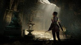 Das Bild zeigt eine mysteriöse Szenerie in einem düsteren Tempel oder einer Höhle. Im Vordergrund steht eine Protagonistin mit einem entschlossenen Blick, die eine Klinge in der Hand hält. Sie trägt eine stilvolle Rüstung, die an asiatische Designtraditionen angelehnt ist. Der Hintergrund ist schwach beleuchtet, mit Lichtstrahlen, die durch Öffnungen in der Decke fallen und die Atmosphäre von Geheimnis und Abenteuer verstärken. Links und rechts sind dekorative Statuen sowie eine Art Laterne zu sehen, die das Setting zusätzlich mystisch wirken lassen. Alles zusammen vermittelt ein Gefühl von Erkundung und Spannung in einer fantastischen Welt.