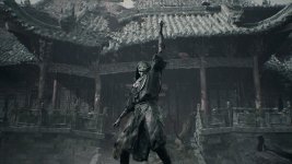 Das Bild zeigt eine mysteriöse Figur, die in einem regnerischen, düsteren Umfeld steht. Die Gestalt trägt einen schlichten, dunklen Umhang und eine auffällige Maske, die eine bedrohliche Ausstrahlung hat. Mit einer erhobenen Hand vermittelt die Figur eine aggressive oder herausfordernde Pose. Im Hintergrund ist ein beeindruckendes, traditionell asiatisches Gebäude zu sehen, dessen verwitterte Struktur und ornamentalen Details eine geheimnisvolle Atmosphäre schaffen. Der Regen und die gedämpften Farben verstärken das Gefühl der Dramatik und der Spannung in der Szene.