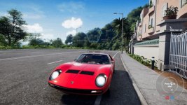 Das Bild zeigt ein rotes Lamborghini Miura auf einer kuppierten Straße, umgeben von üppigem Grün. Die Sonne scheint und der Himmel ist klar mit nur wenigen Wolken. Im Hintergrund sind moderne Gebäude sichtbar, während rechts eine Mauer und ein Tor zu sehen sind. Auf dem Bildschirm sind einige Benutzeroberfläche-Elemente zu erkennen, wie die Option, einen Voice-Chat zu aktivieren, sowie eine Aufforderung, das Spiel zu starten. Die Grafik vermittelt ein lebendiges und einladendes Spielgefühl.