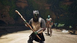 Das Bild zeigt zwei Charaktere aus einem Fantasy-Rollenspiel. Im Vordergrund steht ein Aumaua, der einen Stock als Waffe hält und ein beeindruckendes Outfit trägt. Er hat eine grüne Hautfarbe und spezielle Gesichtszüge, die ihn als Teil seiner Rasse charakterisieren. Im Hintergrund befindet sich ein weiterer Charakter mit blauer Haut, der elegant gekleidet ist und ebenfalls zur Szene beiträgt. Der Hintergrund ist reich an Pflanzen und scheint Teil einer üppigen, fantastischen Umgebung zu sein, die das Setting des Spiels unterstreicht.